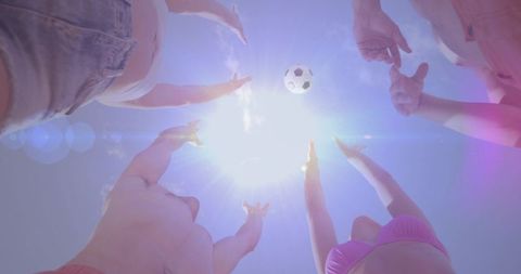 Sunlit friends reaching for soccer ball overhead at beach backlit summer fun