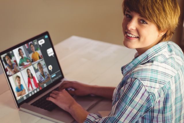 A teenager in casual clothes is smiling while using a laptop for an online class. Several people are shown on the screen participating in the virtual session. Great for illustrating concepts related to e-learning, remote education, online courses, and digital collaboration. Suitable for educational blogs, technology-related articles, and e-learning advertisements.