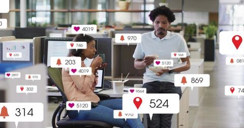 Coworkers sharing coffee amid social media notifications in open-plan coworking office