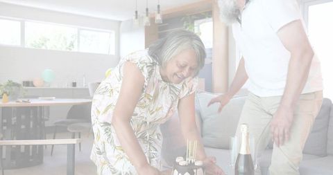 Senior couple preparing birthday celebration with cake and champagne in modern living room