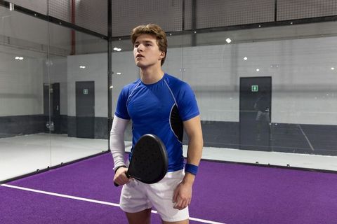 Young athlete holding padel racket on indoor purple court looking focused