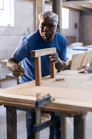 Mature african american carpenter aligning table legs at workbench with safety goggles