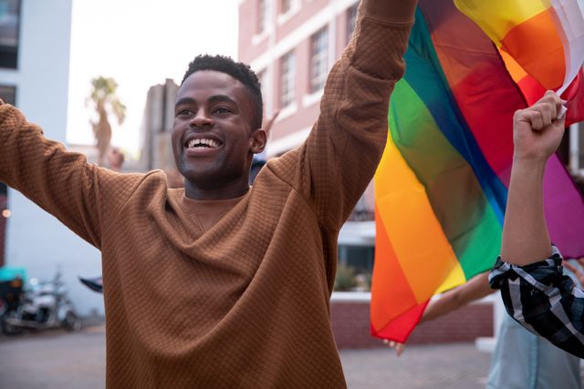 This image captures a joyful African American man holding a rainbow flag during a demonstration. It can be used to represent themes of LGBTQ pride, equal rights, justice, activism, and community celebration. Ideal for articles, social media posts, and campaigns promoting diversity, unity, and empowerment.
