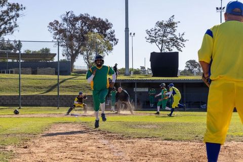 Helmeted runner sprinting to home plate scoring play on amateur baseball field