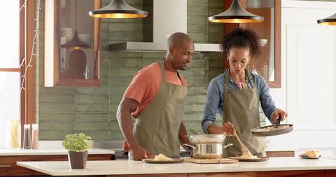 Diverse couple cooking pasta meal in modern kitchen