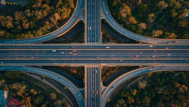Overhead symmetrical highway interchange at golden hour with multi-lane ramps and traffic