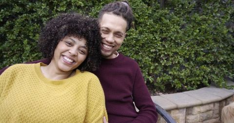 African american couple smiling and leaning on bench in mustard and burgundy knits