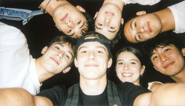 Friends leaning in circle at night smiling with backward cap backpack and denim jacket