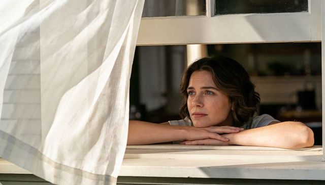 Young woman gazing through open window with breezy curtain, sunlit calm contemplation