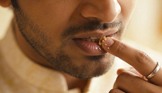 Man tasting crumbs with finger on lower lip closeup, wearing silver ring and beige shirt