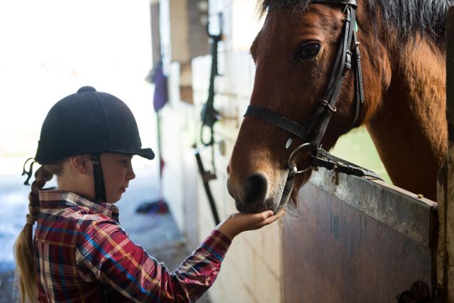 Adorable girl feeding the horse in the stable