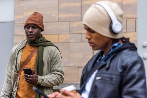 Urban commuters standing on sidewalk checking smartphones while holding takeaway coffee