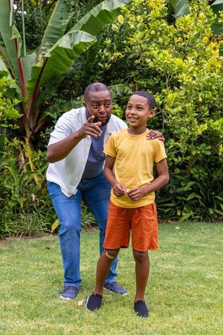 African american father guiding smiling son in tropical backyard garden for family bonding