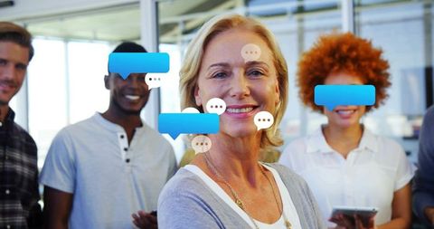 Smiling senior leader guiding diverse team in modern office with digital chat bubbles