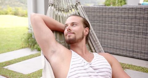 Young man relaxing in backyard hammock on sunny day