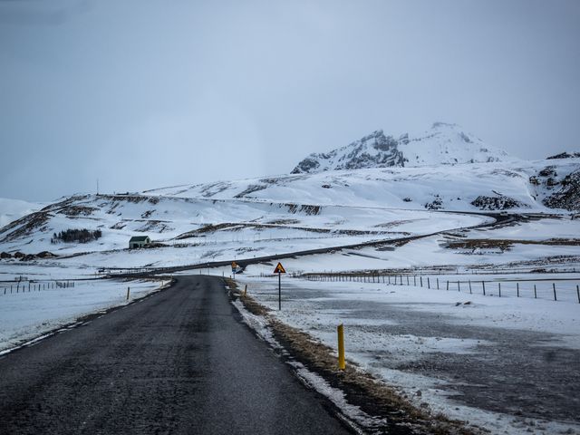 This stock photo depicts an empty road stretching into a snow-covered mountainous region. Ideal for travel brochures, winter destination promotions, or inspirational journey themes. The solitude and stark beauty of the scene can be used for articles on adventure or exploration and travel blogs.