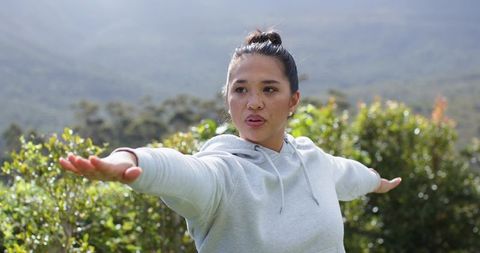 Asian woman stretching arms outdoors on misty hillside