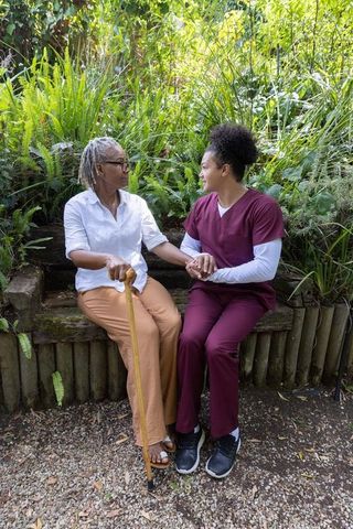 Senior woman and caregiver sitting holding hands on bench in garden compassionate eldercare