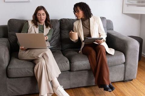 Diverse female coworkers collaborating on laptop and tablet in modern office lounge