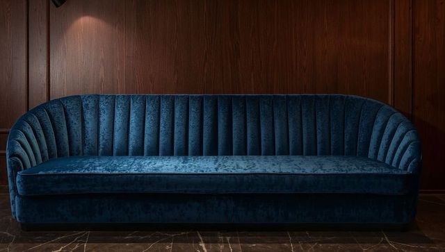 Deep blue velvet channel-tufted sofa showcasing luxe lounge against dark wood paneling