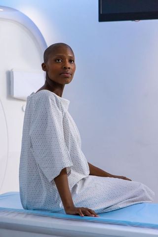 African woman wearing hospital gown sitting before mri scanner, calm patient in radiology
