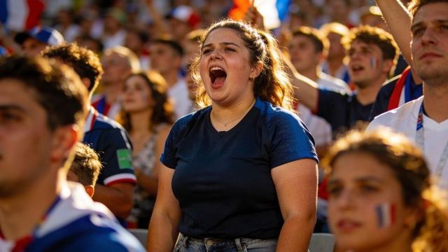 Passionate fan shouting in navy shirt cheering with tricolor flags in stadium crowd