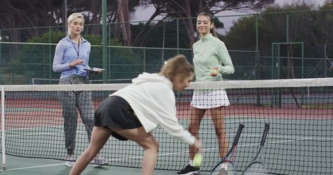 Female tennis coach training young players at net during outdoor practice session