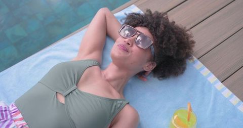 African woman reclining poolside in sage swimsuit and sunglasses, summer relaxation