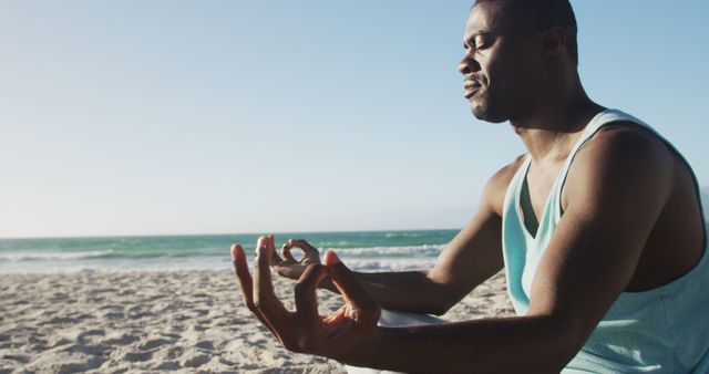 This image features a man meditating in the lotus position on a sunny beach, facing the ocean. Ideal for use in wellness blogs, mindfulness programs, fitness ads, and lifestyle content promoting mental health and relaxation.