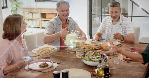 Mature friends sharing homemade dinner and pouring lemonade around wooden table