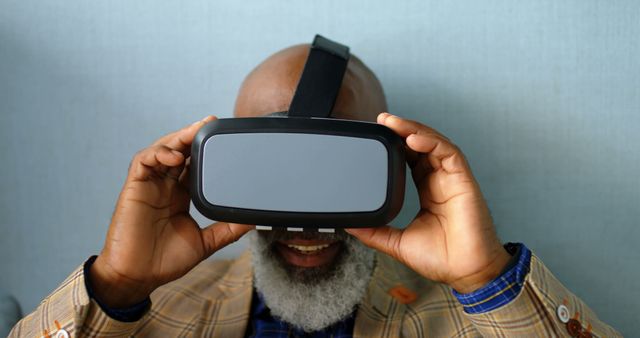 Elderly bearded man smiling while using VR headset, exploring virtual reality technology. Ideal for tech websites, senior engagement in technology, innovation and lifestyle promotions, virtual reality demonstrations and marketing.