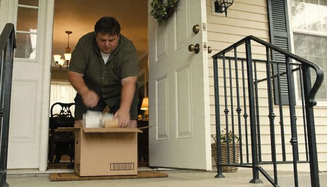 Man unpacking parcel on front porch near open door with wreath and table lamp