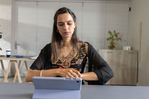 Indian woman working on tablet in minimalist home office wearing embroidered tunic and shawl