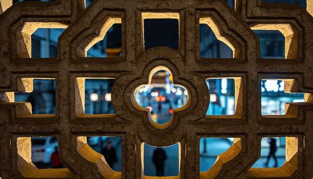 Stone lattice framing warm quatrefoil opening with city bokeh at night