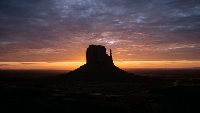 Monumental sunrise silhouette of sandstone butte and spire with winding desert road