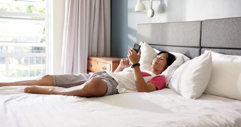 Teen Boy Relaxing on Bed Using Smartphone in Minimalist Bedroom
