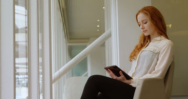 Young woman sitting near window reading e-book on tablet - Download Free Stock Images Pikwizard.com