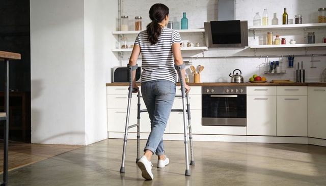 Walking woman using forearm crutches in modern kitchen promoting mobility and independence