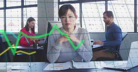 Contemplative Asian woman working at desk with data overlay and line graphs