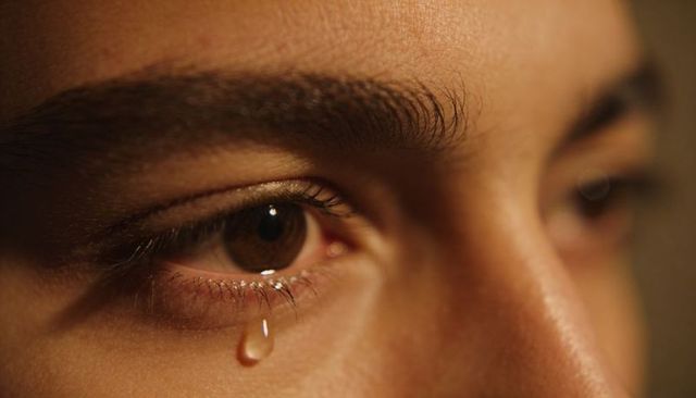 Intimate closeup of brown eye shedding single tear on warm skin with eyelash texture