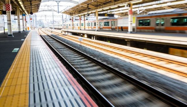 Curving tracks guiding commuters through modern urban train station with motion blur, tactile paving