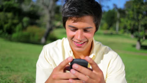 Young Man Smiling While Using Smartphone in Park