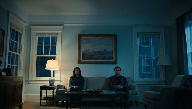 Couple sitting on sofa with hands folded in laps moody blue-toned living room