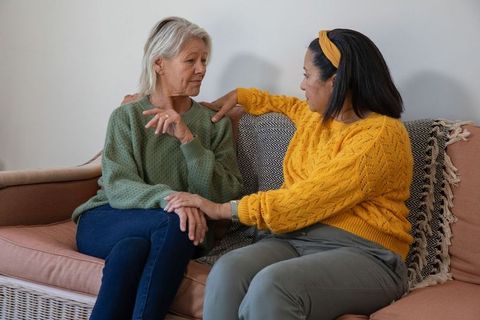 Adult daughter comforting senior woman on sofa conveying empathy and emotional support