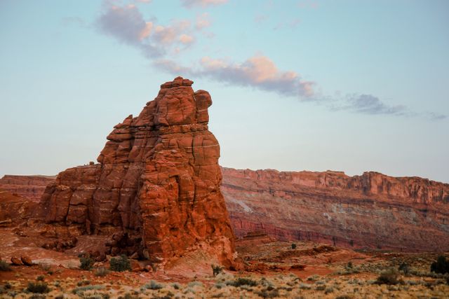 Stunning red rock formation illuminated by sunset light with a clear blue sky and scattered clouds. Perfect for use in travel magazines, educational geology publications, website backgrounds, and landscape postcard designs showcasing natural beauty.