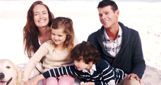 This image captures a happy family of four enjoying time at the beach with their dog. The parents and children are sitting together, smiling, and engaging with each other, showcasing love and unity. Perfect for use in advertising family-oriented products, vacation packages, pet-friendly locations, or lifestyle articles emphasizing family bonds and outdoor activities.