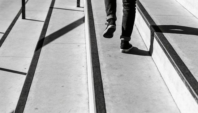 Man walking up concrete steps wearing cuffed pants and sneakers in high-contrast monochrome