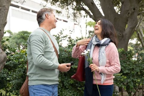 Senior couple laughing in park with daisies and smartphone casual outdoor romance