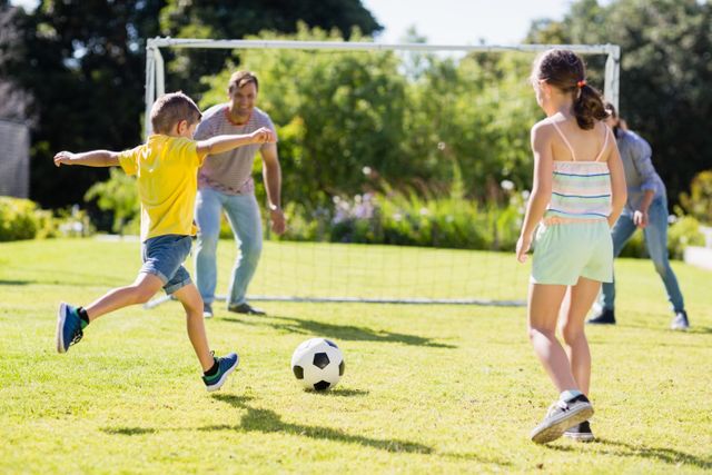 Family enjoying a sunny day playing soccer in a park. Children and parents engaging in outdoor activity, promoting fitness and bonding. Ideal for use in advertisements for family activities, sports equipment, outdoor recreation, and healthy lifestyle promotions.