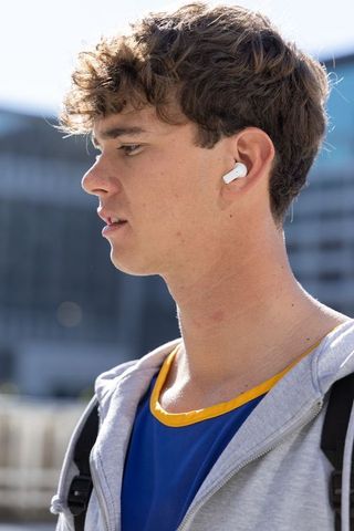 Teen male listening with wireless earbud in urban side-profile portrait, hoodie backpack